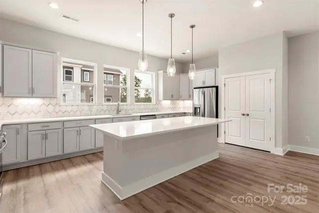 a large kitchen with kitchen island a stove a sink dishwasher a refrigerator and white cabinets with wooden floor