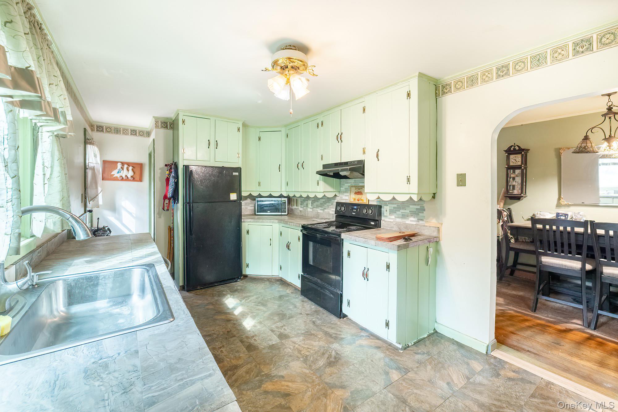 240 Stevers Crossing Road Hudson, NY 12534 - Photo 3 of 21 Kitchen featuring green cabinets, black appliances, light countertops, decorative backsplash, and arched walkways