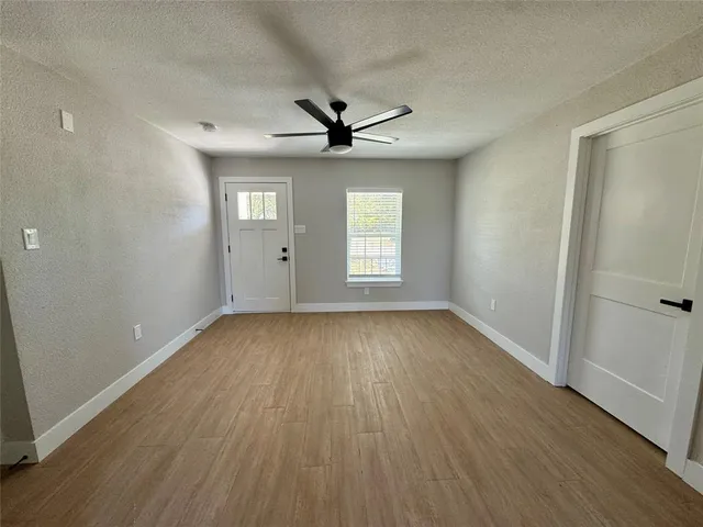 an empty room with wooden floor chandelier fan and windows
