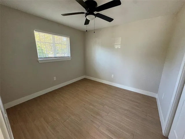 an empty room with wooden floor fan and windows