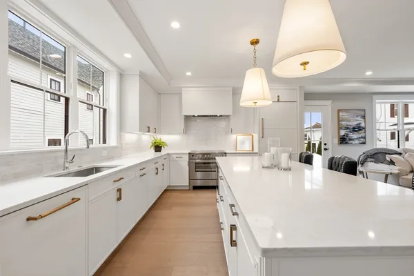 a large white kitchen with a large counter space a sink stainless steel appliances and cabinets