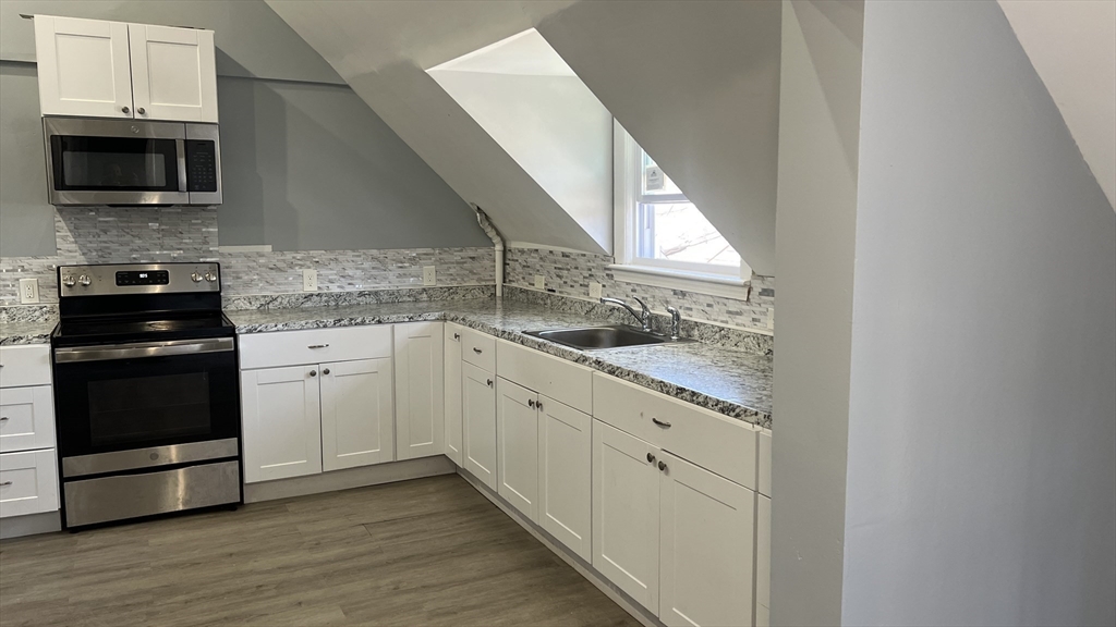 a kitchen with granite countertop white cabinets and a stove with wooden floor