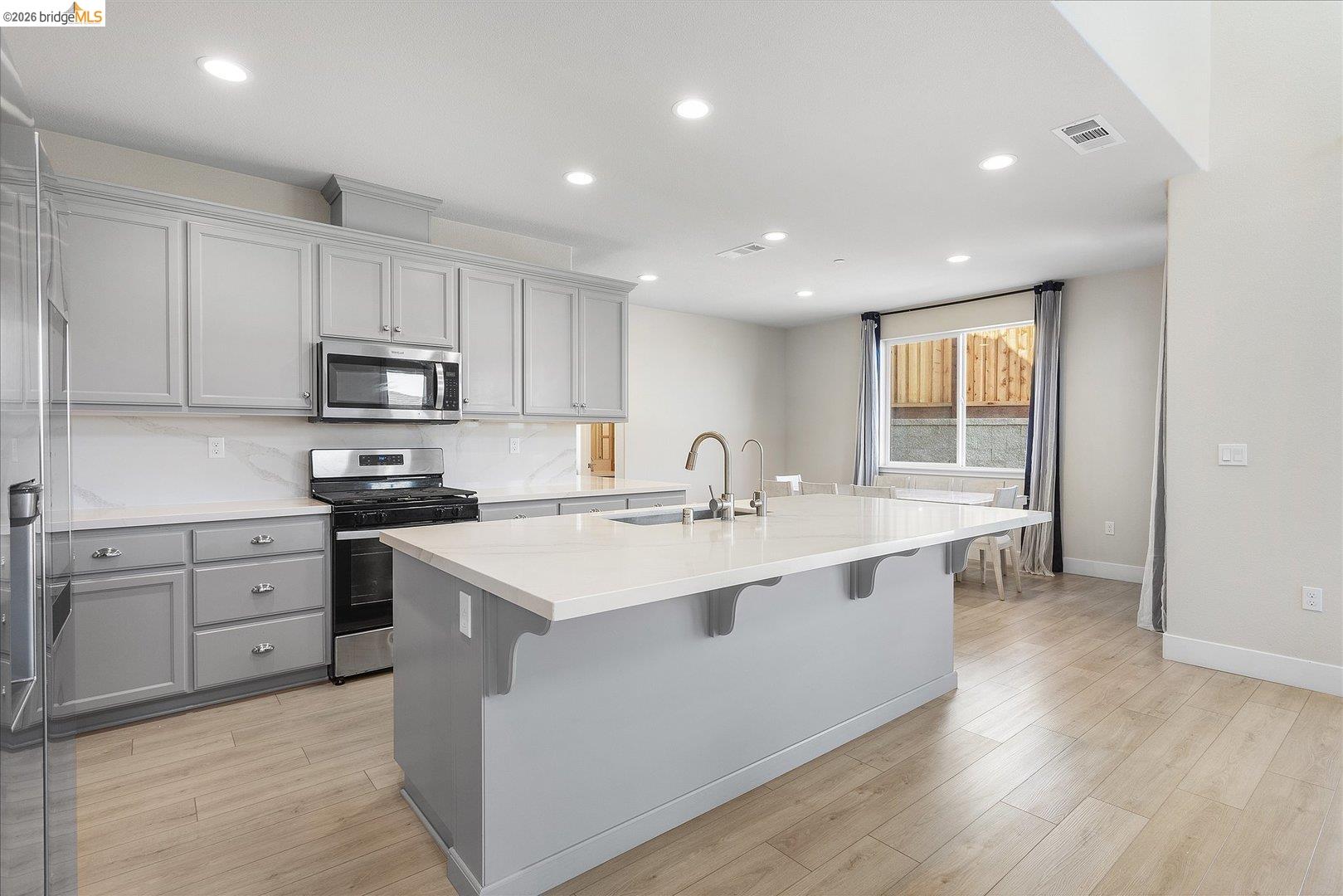 5601 Ridgepoint Way Antioch, CA 94531 - Photo 12 of 59 Modern kitchen featuring an expansive center island with an integrated sink, light-toned cabinetry, stainless steel appliances, recessed lighting, and wood-finish flooring
