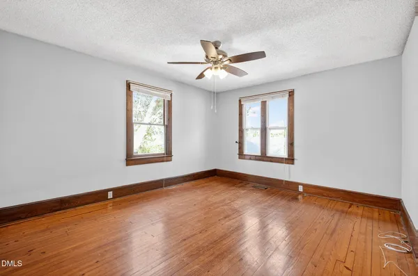 an empty room with wooden floor chandelier fan and windows