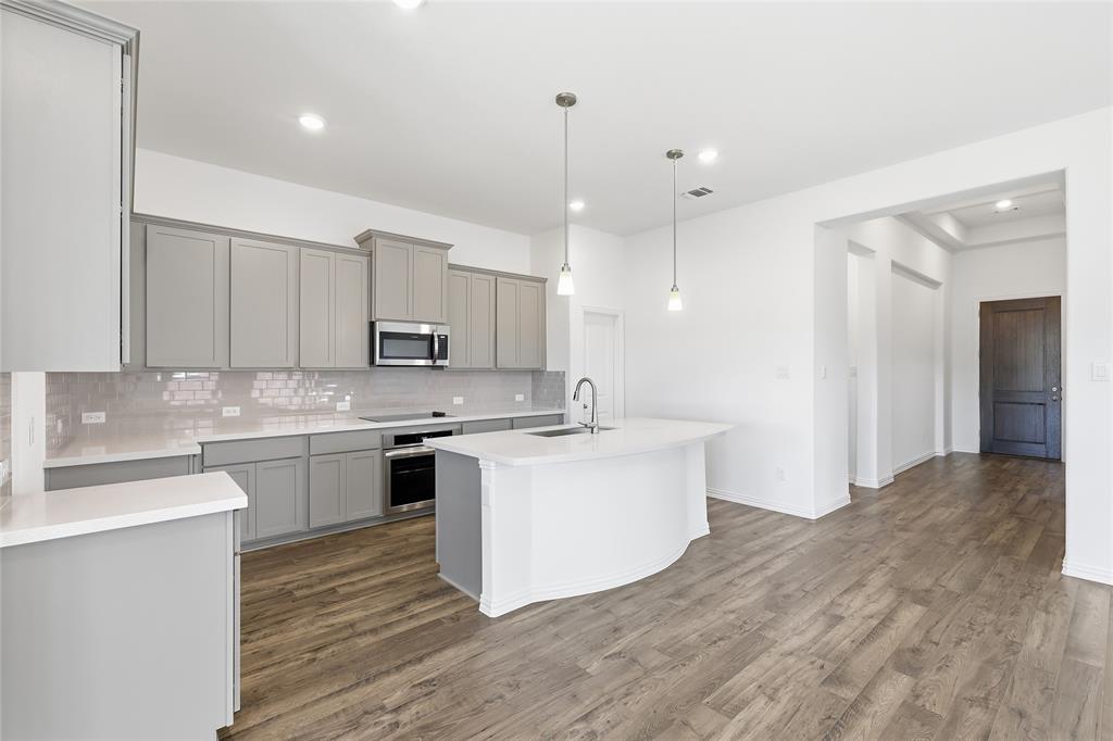 2529 Rivers W Road Anna, TX 75409 - Photo 12 of 40 Modern kitchen featuring wood-finish flooring, light gray cabinetry, white countertops, a subway tile backsplash, and a curved island with pendant lighting