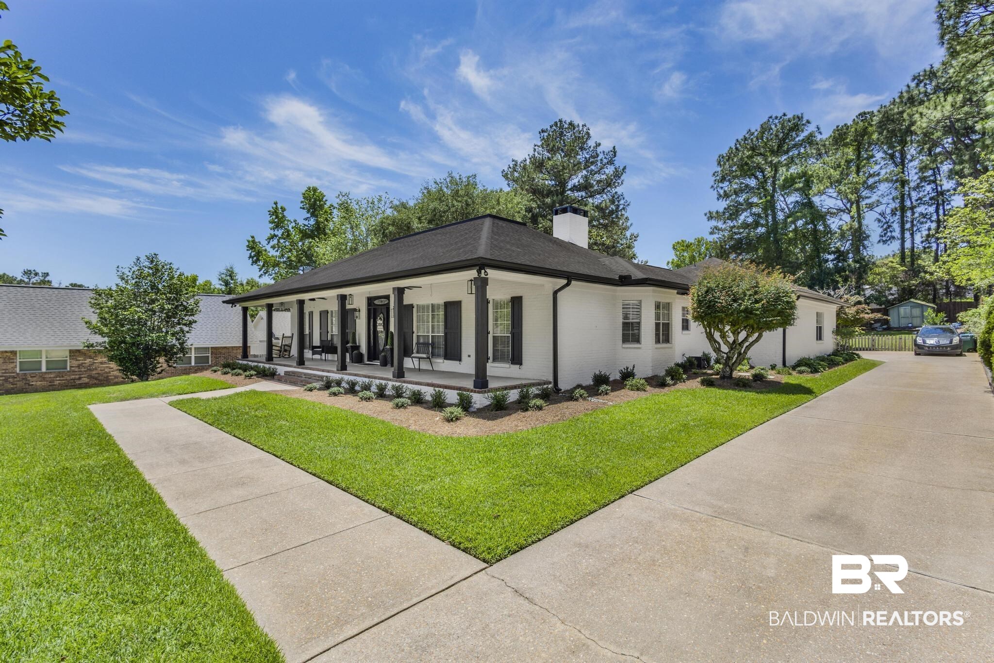 83 Caisson Trace Daphne, AL 36527 - Photo 4 of 63 White painted brick exterior with a deep covered front porch, black architectural shingle roof, black shutters, and mature landscaping