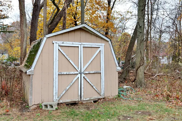 a view of a white house in front of a big yard with plants and large trees