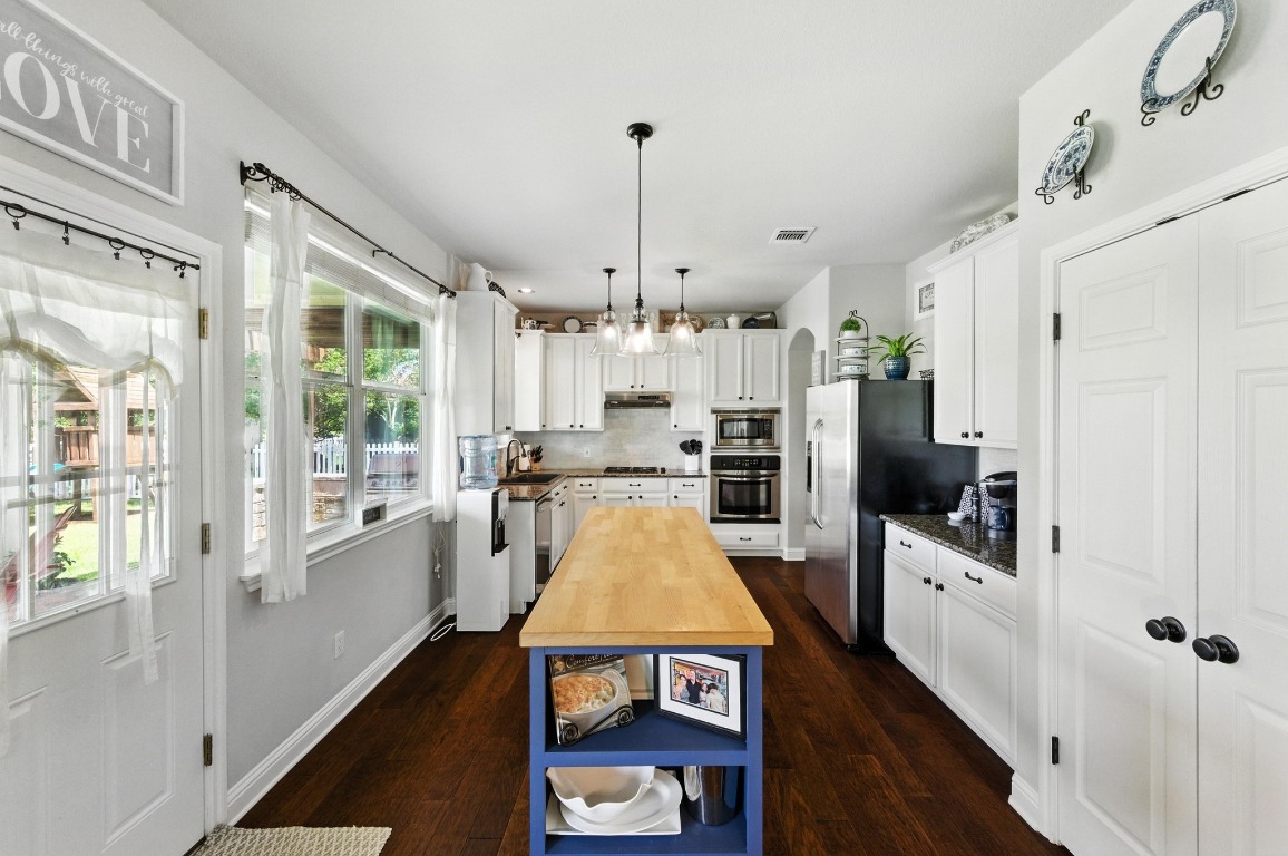 316 Caraway Kyle, TX 78640 - Photo 13 of 39 Kitchen featuring granite counters, custom island, wood floors, white cabinetry, and stainless steel appliances