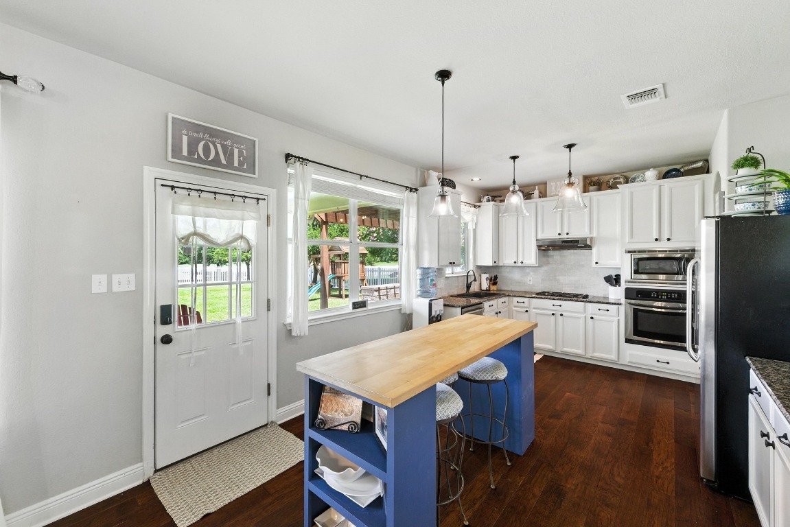 316 Caraway Kyle, TX 78640 - Photo 14 of 39 Kitchen featuring wood flooring, appliances with stainless steel finishes, butcher granite countertops, white cabinets, and backsplash