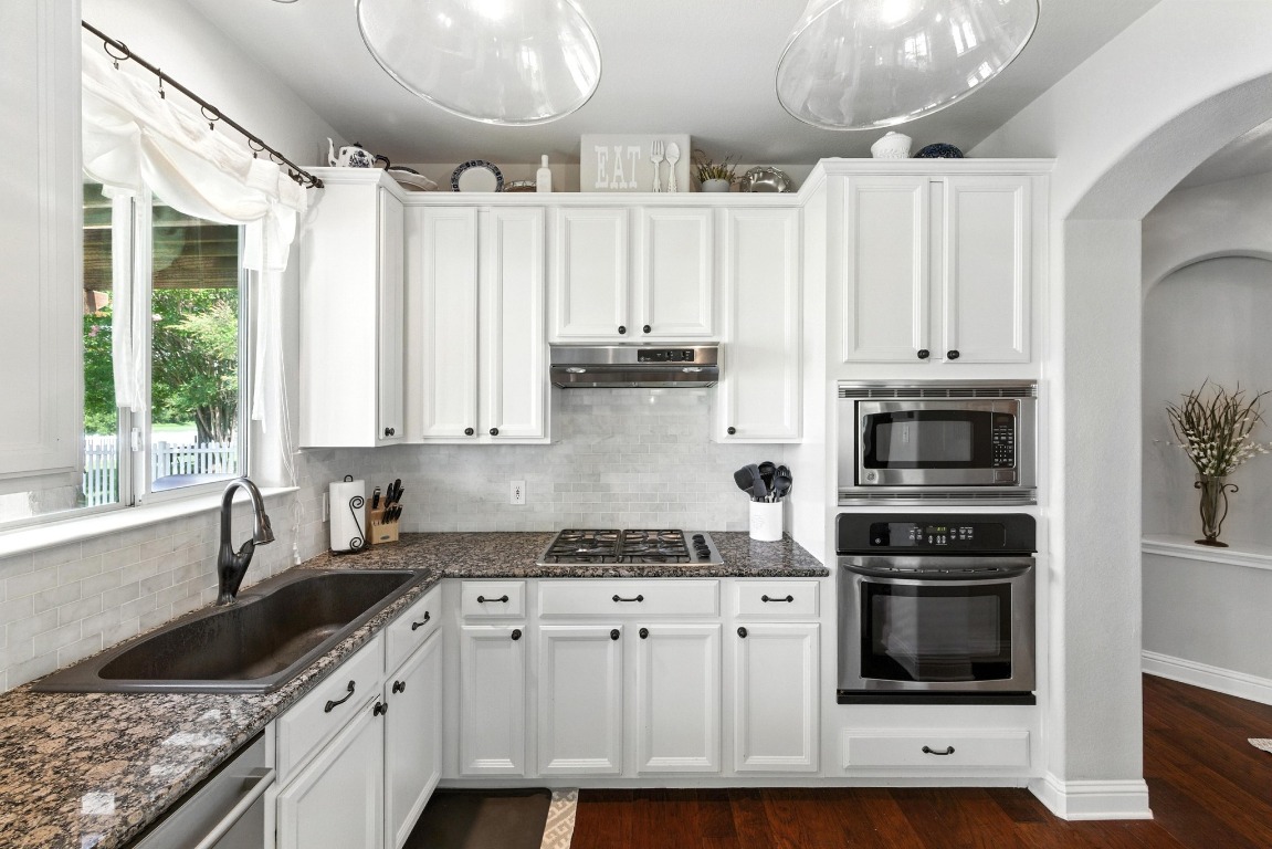 316 Caraway Kyle, TX 78640 - Photo 16 of 39 Kitchen featuring stainless steel appliances, arched walkways, tasteful backsplash, white cabinetry, and wood flooring