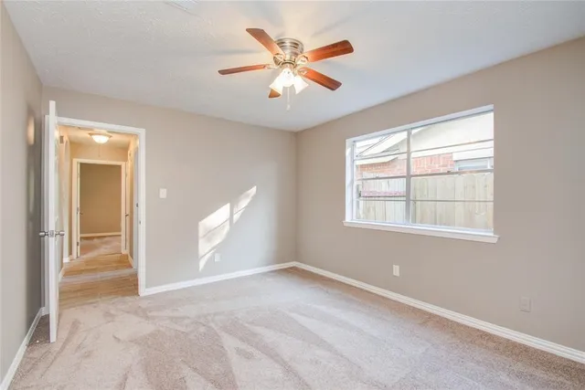 an empty room with chandelier fan and windows