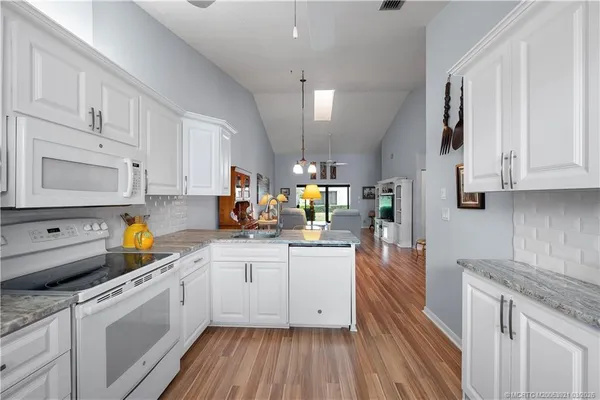 a kitchen with stainless steel appliances granite countertop a sink dishwasher stove and white cabinets with wooden floor