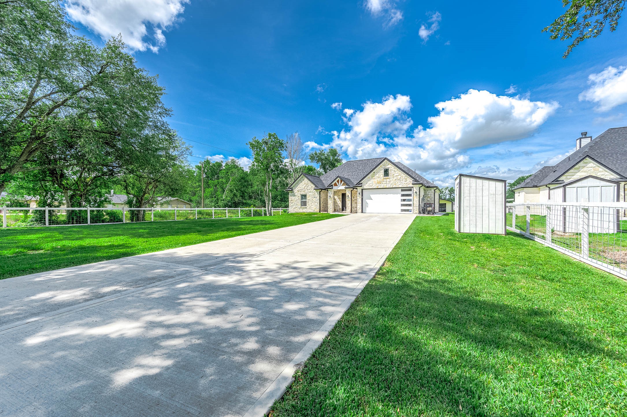 8032 Short Road Needville, TX 77461 - Photo 2 of 50 A different angle of the front of the home showcasing the spacious driveway leading to the attached two-car garage. Surrounded by a lush green lawn and mature trees, this property offers a peaceful setting with the perfect blend of modern design and country charm on a beautiful 1-acre tract.