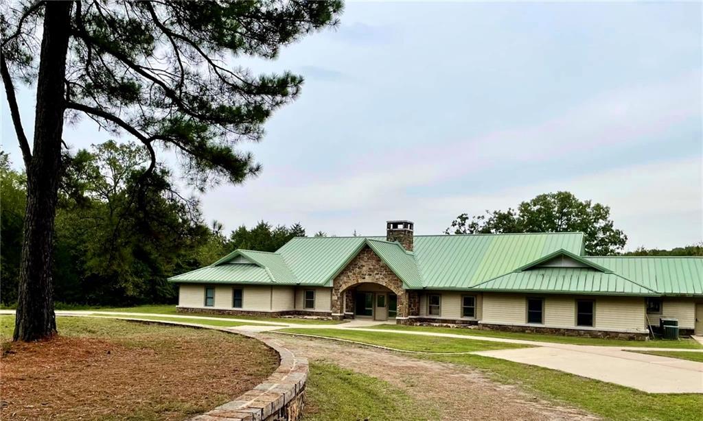 8524 Youth Ranch Road Mulberry, AR 72947 - Photo 30 of 40 Ranch-style residence featuring a prominent green metal roof, stone facade accents, a stone chimney, and a curved paved driveway