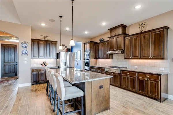 a kitchen with stainless steel appliances kitchen island granite countertop a stove a sink a refrigerator and chairs