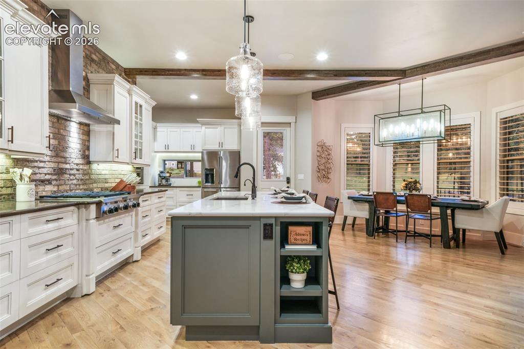 18572 Wetherill Road Monument, CO 80132 - Photo 17 of 50 Open-concept kitchen and dining area featuring light wood-finish flooring, a kitchen island with built-in shelving and white countertop, white cabinetry, and a brick-finish backsplash