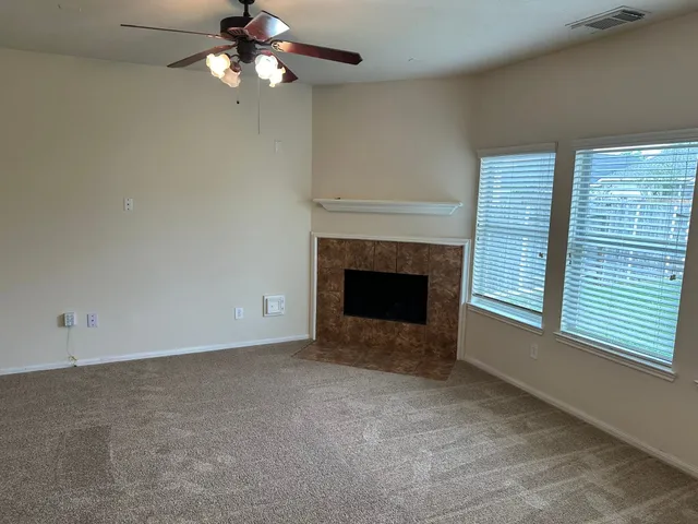 a view of a livingroom with a fireplace a ceiling fan and windows