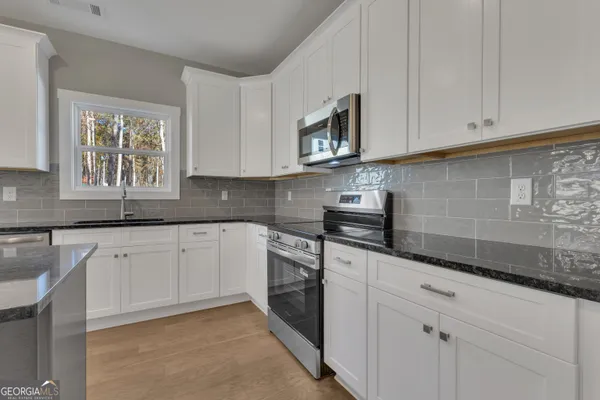 a kitchen with stainless steel appliances granite countertop a stove top oven a sink and white cabinets