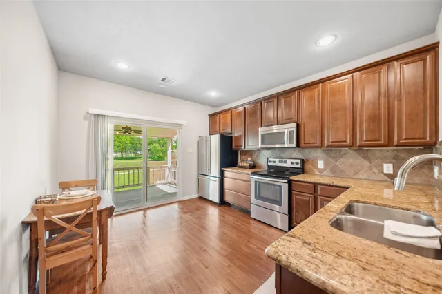 a kitchen with stainless steel appliances granite countertop wooden cabinets a stove top oven a sink and dishwasher a dining table with wooden floor