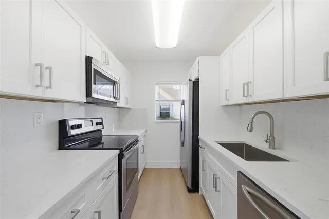 a kitchen with stainless steel appliances a sink a stove a microwave a refrigerator a counter space and cabinets