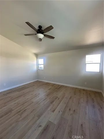 an empty room with wooden floor fan and windows