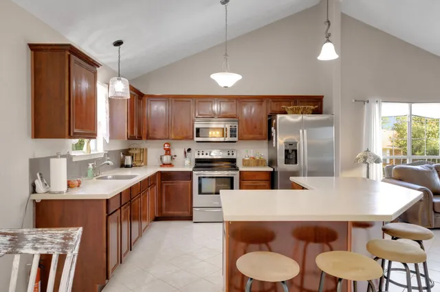 a kitchen with stainless steel appliances granite countertop a sink a stove a refrigerator cabinets and a dining table
