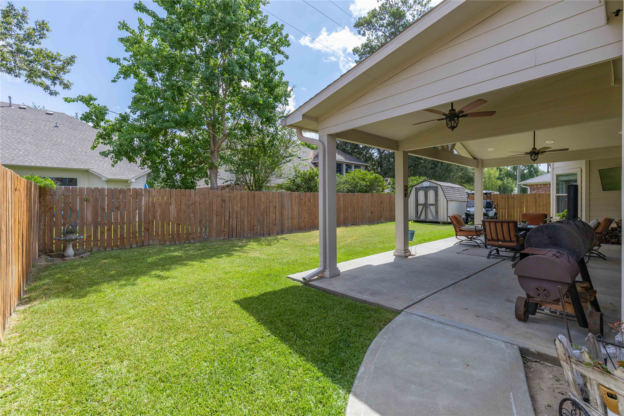24506 Fort Path Drive Spring, TX 77373 - Photo 43 of 46 Spacious backyard with a covered patio featuring ceiling fans, perfect for outdoor entertaining and relaxation.