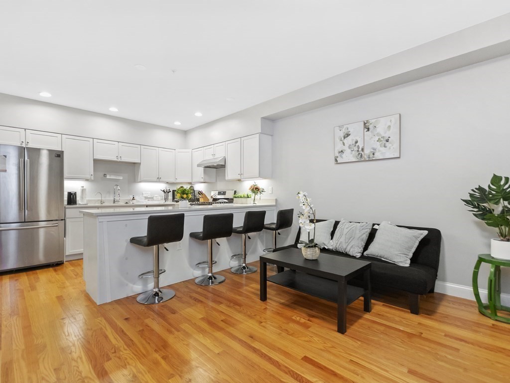 a living room with stainless steel appliances kitchen island a table chairs and a refrigerator