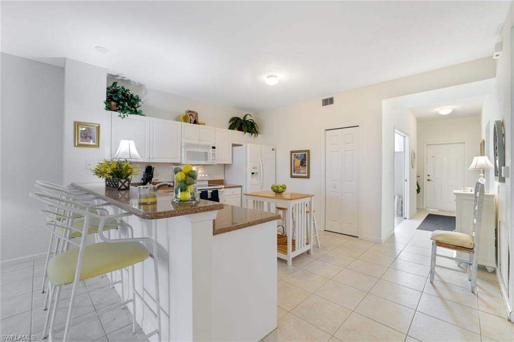10049 Heather Lane, Unit 101 Naples, FL 34119 - Photo 10 of 28 Kitchen with white cabinets, light tile patterned flooring, a breakfast bar area, and white appliances