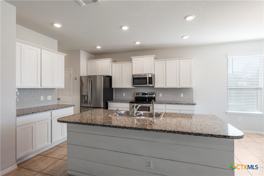 1129 Ibis Falls Loop Jarrell, TX 76537 - Photo 18 of 39 a kitchen with granite countertop stainless steel appliances a sink a stove a microwave a refrigerator and cabinets