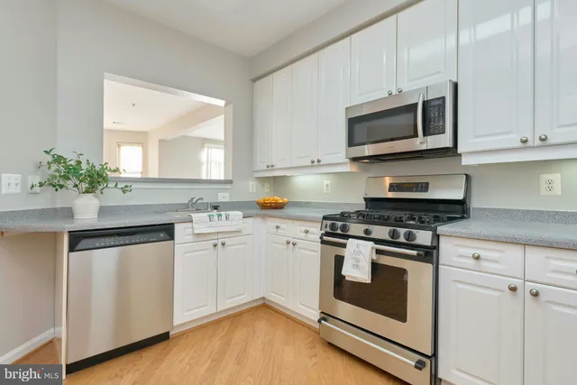 a kitchen with granite countertop white cabinets stainless steel appliances and wooden floor