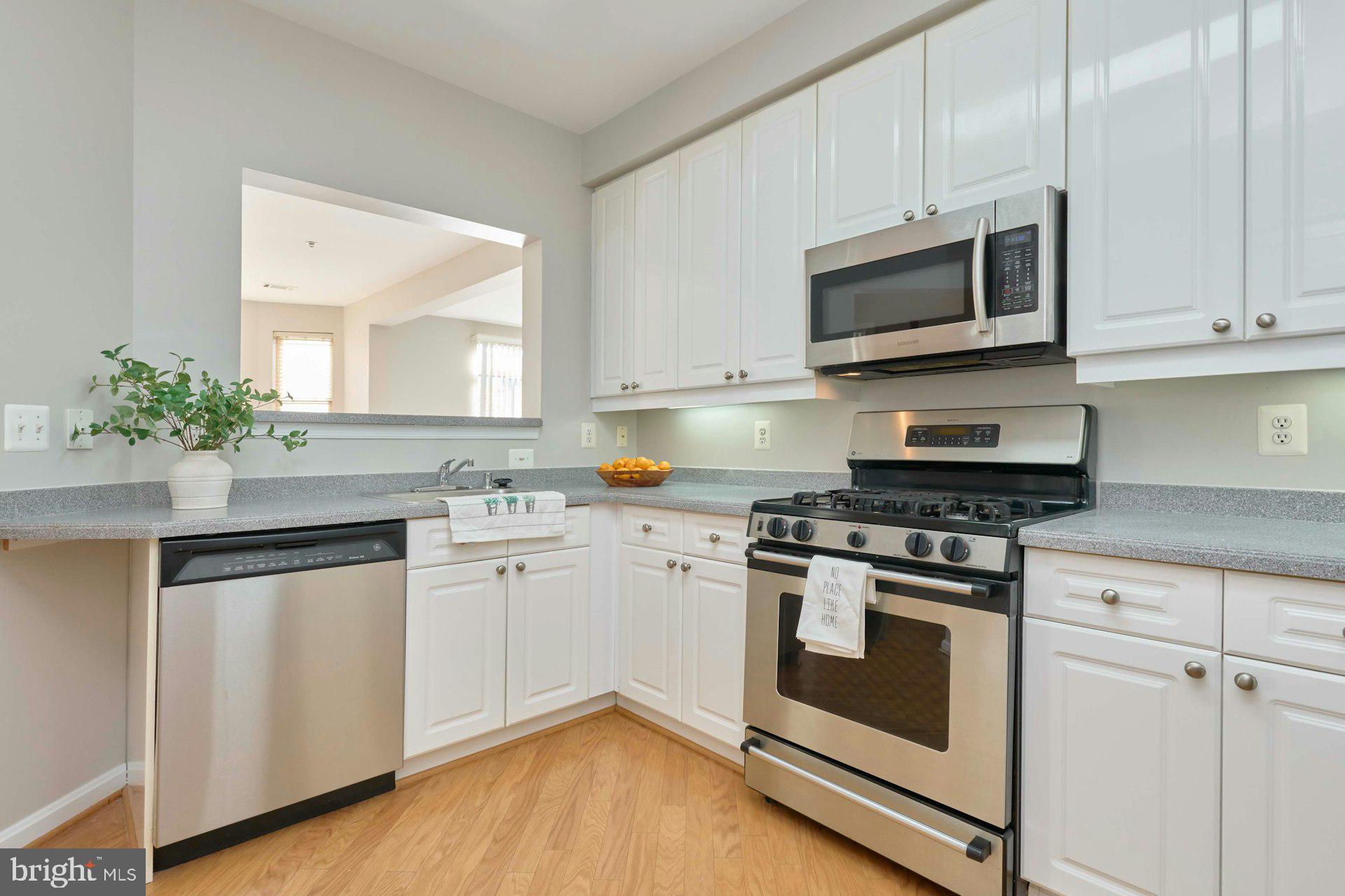 1851 Stratford Park Place, Unit 212 Reston, VA 20190 - Photo 11 of 40 a kitchen with granite countertop white cabinets stainless steel appliances and wooden floor