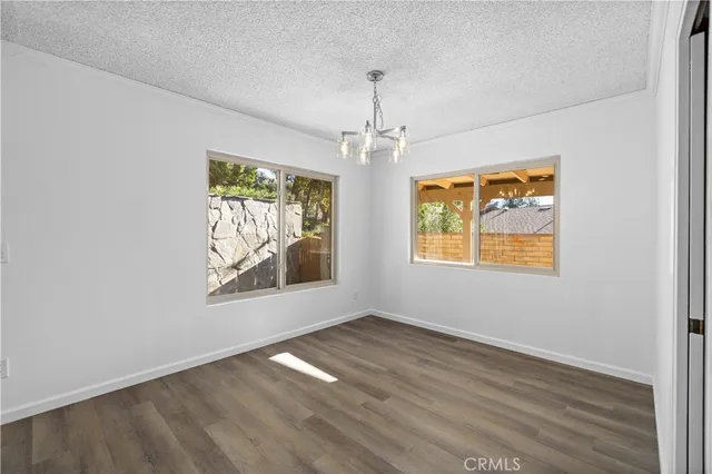 an empty room with wooden floor chandelier and windows