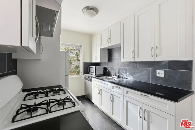 a kitchen with granite countertop a sink stove and white cabinets