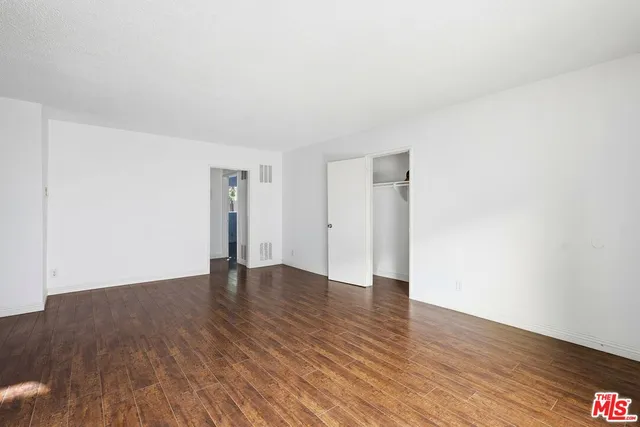 a view of an empty room with wooden floor and closet