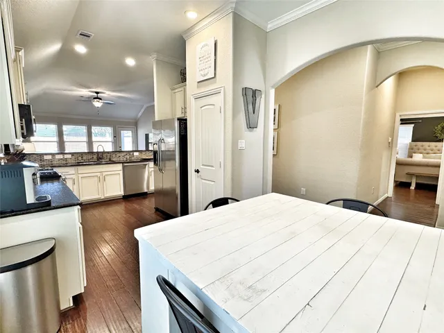 a kitchen with stainless steel appliances kitchen island granite countertop a refrigerator a stove and white cabinets with wooden floor