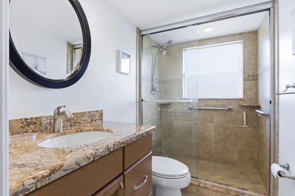 a bathroom with a granite countertop sink a mirror a toilet and a shower