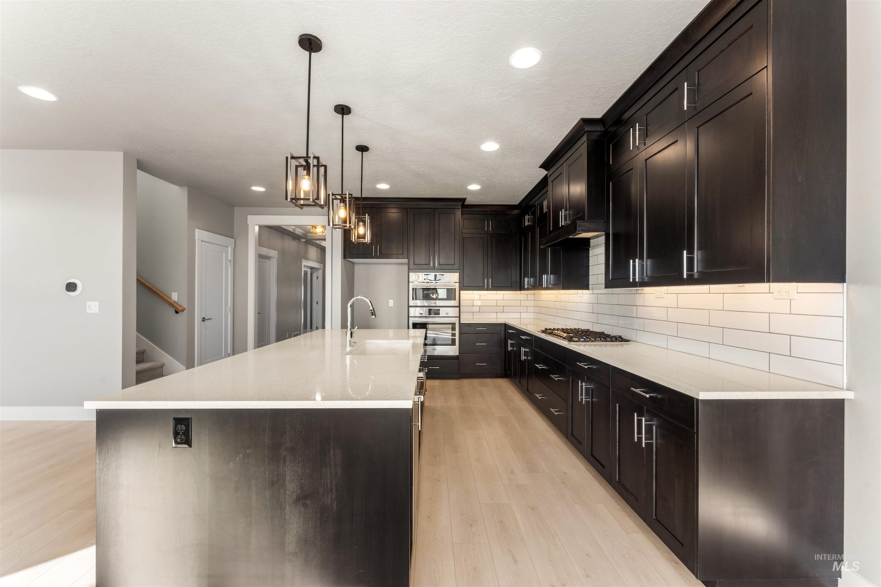 8081 Tandy Cove Street Middleton, ID 83644 - Photo 6 of 41 Kitchen featuring light stone countertops, light wood-style floors, pendant lighting, backsplash, and a center island with sink