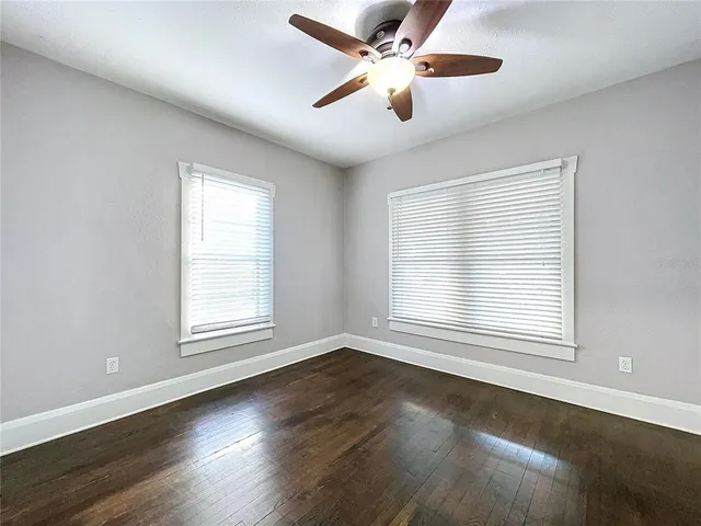 an empty room with wooden floor chandelier fan and windows