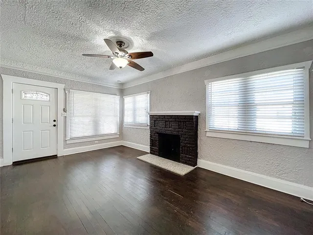 an empty room with wooden floor fireplace and windows