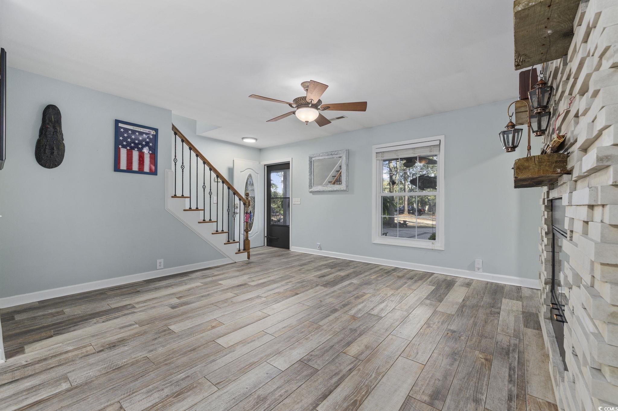 153 Watson Way Pawleys Island, SC 29585 - Photo 5 of 40 Unfurnished living room featuring stairway, a fireplace, light wood-style floors, and ceiling fan