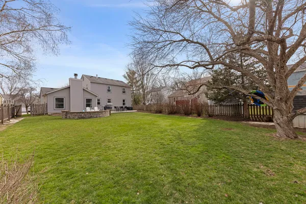 a view of a white house next to a yard with a large tree