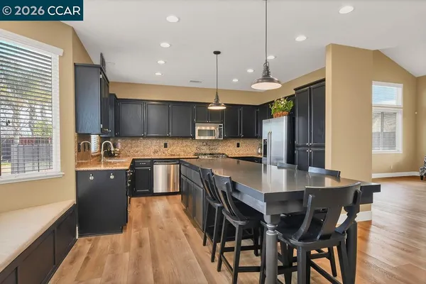 a kitchen with stainless steel appliances granite countertop a stove top oven a sink dishwasher a dining table and chairs with wooden floor