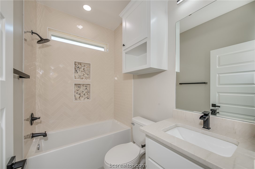 2908 GOLDBERG Drive Bryan, TX 77808 - Photo 9 of 44 Guest bath room features plate mirror, decorative light fixture, tiled tub/ shower combination with shampoo boxes, and painted cabinets with quartz countertop and plate mirror.