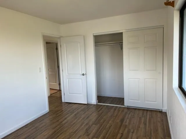 a view of an empty room with wooden floor and closet