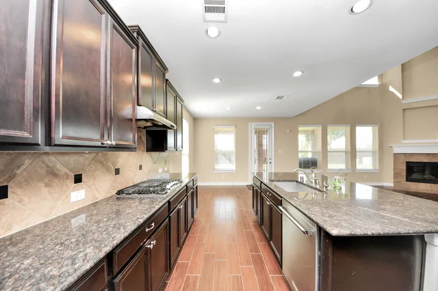 a kitchen with stainless steel appliances granite countertop a sink a stove and a wooden floors