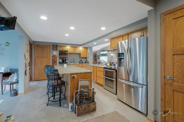 a kitchen with stainless steel appliances kitchen island granite countertop a refrigerator a table and chairs