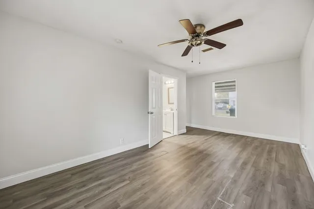 an empty room with wooden floor a ceiling fan and windows
