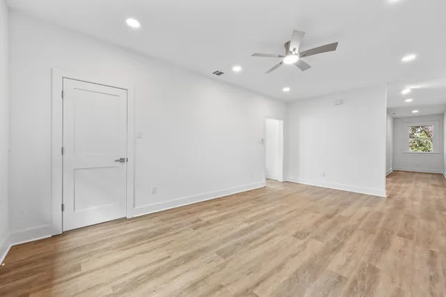 a view of an empty room with wooden floor and a ceiling fan