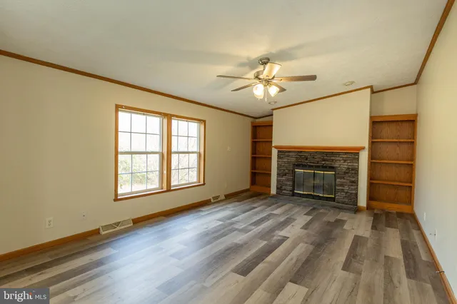 a view of a livingroom with a fireplace a ceiling fan and wooden floor